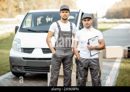 Porträt einer zwei Lieferung Männer in Uniform stehen zusammen mit Checkliste und Kartons in der Nähe der Cargo van Fahrzeug im Freien Stockfoto