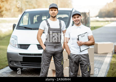 Porträt einer zwei Lieferung Männer in Uniform stehen zusammen mit Checkliste und Kartons in der Nähe der Cargo van Fahrzeug im Freien Stockfoto