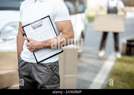 Lieferung Mann mit chek Liste in der Nähe des Auto und Pakete im Freien, close-up auf einem Klemmbrett Stockfoto