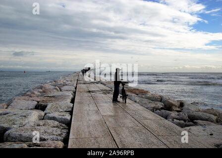 novenber 13, 2019.Adriaküste vonVenetien, Strand Sottomarina. Schlechtes Wetter, Wind- und Seesturm trafen die Küste. Ein Biker am Kai entlang. Stockfoto