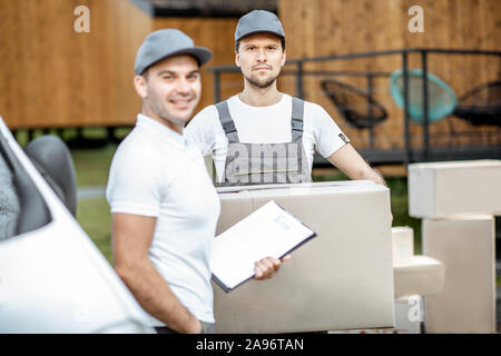 Porträt einer zwei Lieferung Männer in Uniform stehen zusammen mit Checkliste und Kartons in der Nähe der Cargo van Fahrzeug im Freien Stockfoto