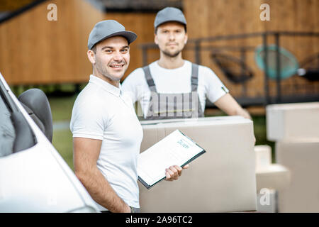 Porträt einer zwei Lieferung Männer in Uniform stehen zusammen mit Checkliste und Kartons in der Nähe der Cargo van Fahrzeug im Freien Stockfoto