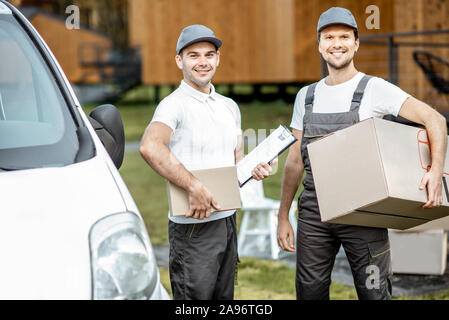 Porträt einer zwei freundliche Lieferung Männer in Uniform stehen zusammen mit Checkliste und Kartons in der Nähe der Cargo van Fahrzeug im Freien Stockfoto