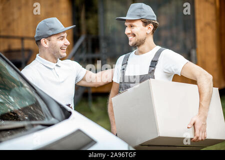 Porträt einer zwei Lieferung Männer in Uniform stehen zusammen mit Checkliste und Kartons in der Nähe der Cargo van Fahrzeug im Freien Stockfoto