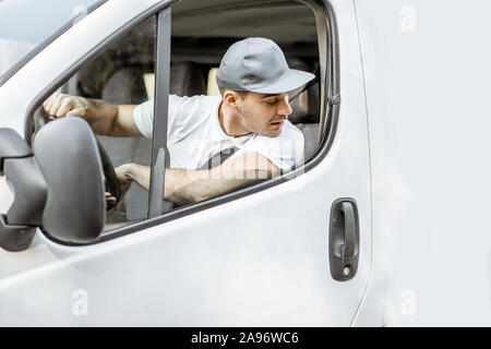 Porträt einer fröhlichen Anlieferung Treiber in Uniform Blick aus dem Fenster des weißen Lieferwagen vahicle, Lieferung mit dem Auto Stockfoto