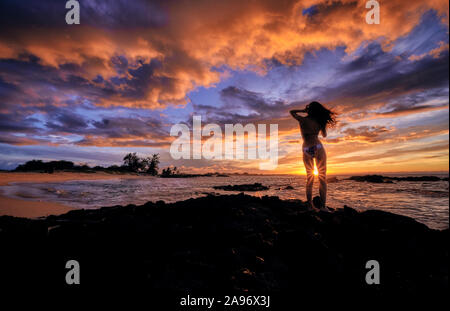Eine junge Frau hält den Sonnenuntergang auf Makalawena Beach Hawaii zu feiern. Stockfoto