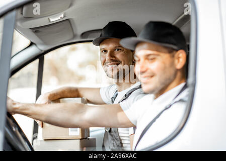 Zwei freundliche Lieferung Unternehmen Mitarbeiter in Uniform Spaß beim Fahren einer Ladung Fahrzeug, die Ware an den Kunden Stockfoto