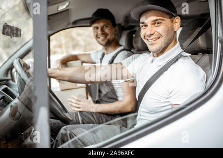 Zwei freundliche Lieferung Unternehmen Mitarbeiter in Uniform Spaß beim Fahren einer Ladung Fahrzeug, die Ware an den Kunden Stockfoto