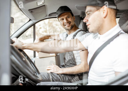 Zwei freundliche Lieferung Unternehmen Mitarbeiter in Uniform Spaß beim Fahren einer Ladung Fahrzeug, die Ware an den Kunden Stockfoto