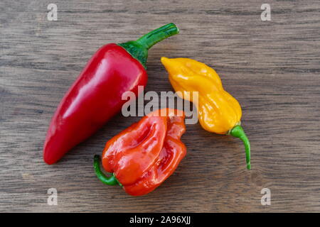 Drei frische organische Paprika, rot, orange und gelb Peperoni auf einem hölzernen Tisch von oben betrachtet, Habanero, fatali, cayenne Stockfoto