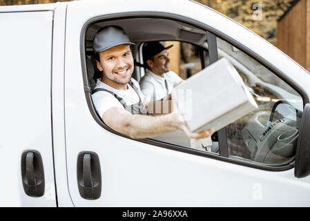 Freundliche Lieferung Mitarbeiter in Unternehmen, die Ware an den Kunden auf einer Ladung Fahrzeug, stattlich Kurier Blick aus dem Fenster mit einem Paket Stockfoto