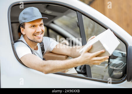 Freundliche Lieferung Mitarbeiter in Unternehmen, die Ware an den Kunden auf einer Ladung Fahrzeug, stattlich Kurier Blick aus dem Fenster mit einem Paket Stockfoto