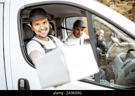 Freundliche Lieferung Mitarbeiter in Unternehmen, die Ware an den Kunden auf einer Ladung Fahrzeug, stattlich Kurier Blick aus dem Fenster mit einem Paket Stockfoto