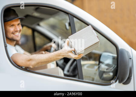 Freundliche Lieferung Mitarbeiter in Unternehmen, die Ware an den Kunden auf einer Ladung Fahrzeug, stattlich Kurier Blick aus dem Fenster mit einem Paket Stockfoto
