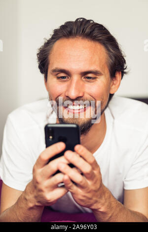 Foto von einem gutaussehenden jungen Mann, der lächelt, während sein Handy zu halten. Stockfoto