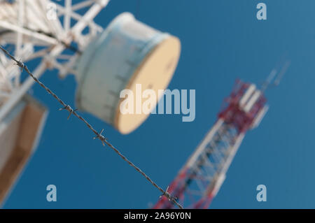 Stacheldraht im Fokus mit Kommunikation Türme und blauer Himmel im Hintergrund. Telekommunikation, Technologie, LTE, 4G, 5G, 6G Stockfoto