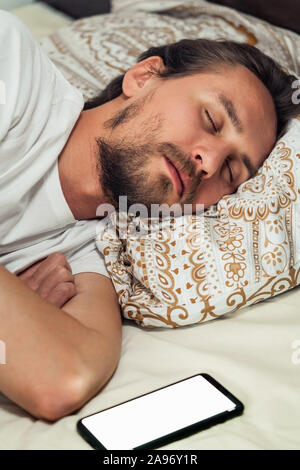 Telefon im Bett neben einem gutaussehenden jungen Mann, dass ist ein Nickerchen. Bildschirm des Telefons eingeschaltet ist. Stockfoto