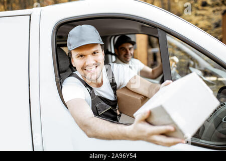 Freundliche Lieferung Mitarbeiter in Unternehmen, die Ware an den Kunden auf einer Ladung Fahrzeug, stattlich Kurier Blick aus dem Fenster mit einem Paket Stockfoto