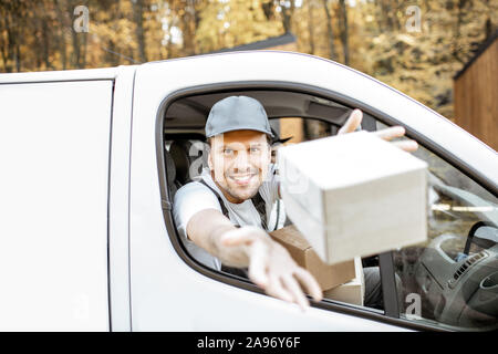 Freundliche Lieferung Mitarbeiter in Unternehmen, die Ware an den Kunden auf einer Ladung Fahrzeug, stattlich Kurier Blick aus dem Autofenster, werfen ein Paket Stockfoto