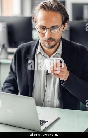 Jungen gutaussehenden Mann Kaffee trinken während der Arbeit am PC-Arbeitsplatz. Stockfoto