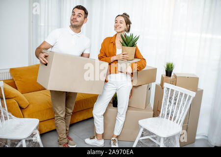 Portrait von ein glückliches junges Paar stehen zusammen mit Boxen und neuen Möbeln im hellen Wohnzimmer. Konzept der Umzug in ein neues Zuhause. Stockfoto