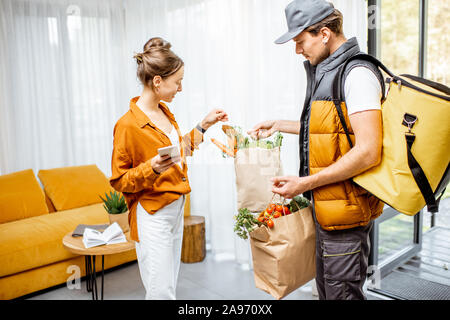 Courier in Uniform mit thermischen Tasche liefert frische Lebensmittel in Tüten zu einem Client Home. Frauen, die ihre Online Bestellung Stockfoto