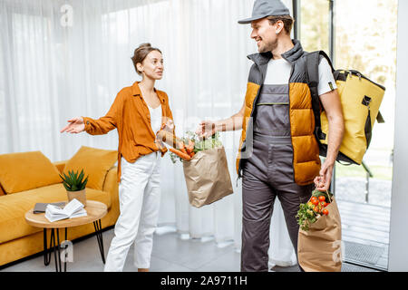 Courier in Uniform liefert frische Lebensmittel Home für eine junge Kunden. Online Shopping und Home delivery Konzept Stockfoto