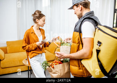 Courier in Uniform mit thermischen Tasche liefert frische Lebensmittel in Tüten zu einem Client Home. Frauen, die ihre Online Bestellung Stockfoto