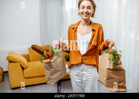 Portrait einer jungen Frau, die mit frischen Lebensmitteln in Tüten zu Hause Stockfoto