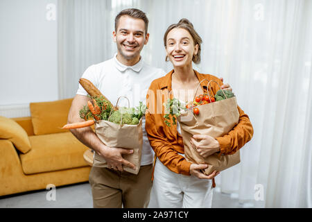 Portrait einer jungen und freundlichen Paar stehend mit frischen Lebensmitteln in Tüten zu Hause Stockfoto