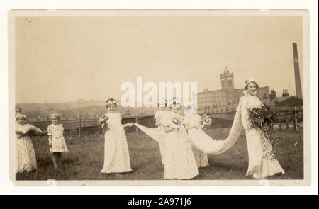 Originalfoto des Karnevals der Rosenkönigin aus dem frühen 20. Jahrhundert von der St. Thomas School, Halliwell, Bolton - hier mit der frisch gekrönten Rosenkönigin und ihren Begleitern, die den Zug ihres Kleides halten, an einem traditionellen „Walking Day“. Die Baumwollfabrik von Falcon befindet sich im Hintergrund, Greater Manchester, Großbritannien, um 1940 Stockfoto