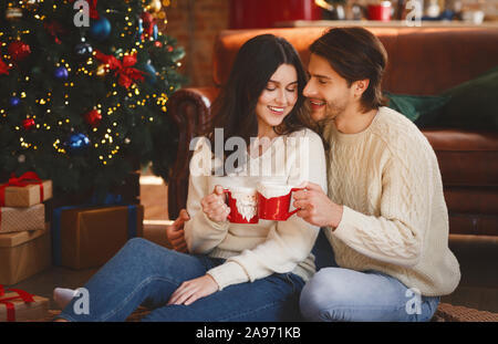 Verliebtes Paar in xmas Kakao neben Weihnachtsbaum zu Hause, freier Speicherplatz Stockfoto