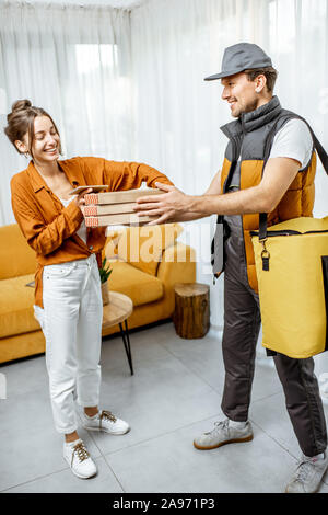 Stattliche Kurier in Uniform liefern Pizza mit thermischen Beutel an einen Client zu Hause, glücklich, Frau ihre Bestellung empfangen Stockfoto