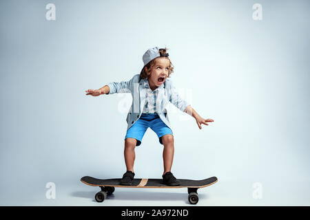 Hübsche junge Junge auf Skateboard in Freizeitkleidung auf weißem Studiohintergrund. Reiten und sieht glücklich aus. Kaukasier Männlich Vorschüler mit hellen Gesichts Emotionen. Kindheit, Ausdruck, Spaß zu haben. Stockfoto