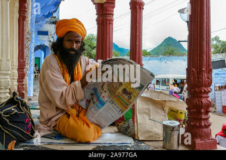 Pushkar, Rajasthan, Indien: Porträt eines Sadhu lesen eine Zeitung unter dem Eingangsportal der Rangji Tempel Stockfoto