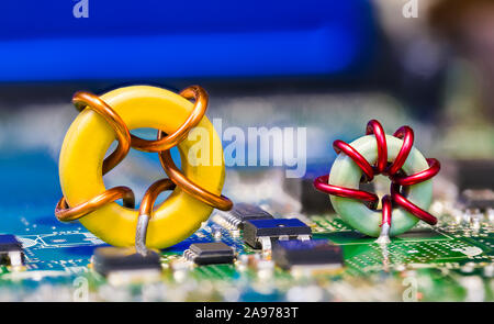 Zwei farbige toroidal Induktionsspulen auf grün blau Platine detail. Runde Magnetkern Induktivitäten mit Kupferdraht Wicklung. Elektronische Komponenten. Stockfoto