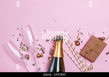 Kreative Zusammensetzung mit einer Flasche Champagner, 2 Sektgläser, gold Flitter und Konfetti auf rosa Hintergrund Stockfoto