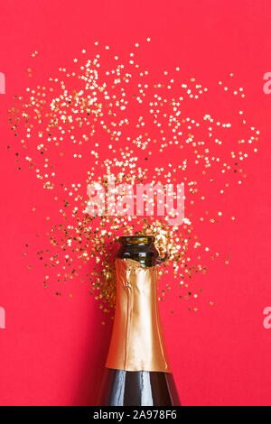 Champagner Flasche mit Golden Star geformt Konfetti auf rotem Hintergrund. Stockfoto