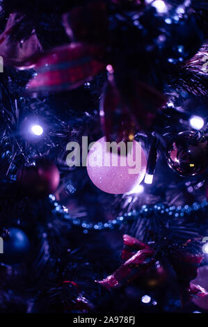 Geschmückten Weihnachtsbaum close-up in Neon Blau Licht. Spielzeug Bälle und Girlande mit Beleuchtung mit Laternen. New Year's baubles Makro Foto mit Bokeh Stockfoto