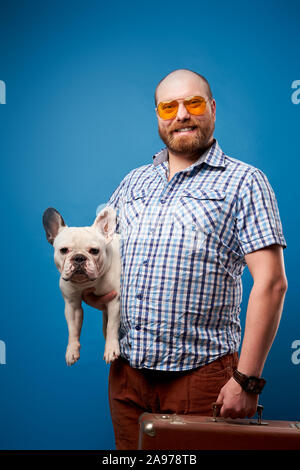 Glatzköpfige Mann mit Hund und Gepäck auf leeren blauen Hintergrund im Studio Stockfoto