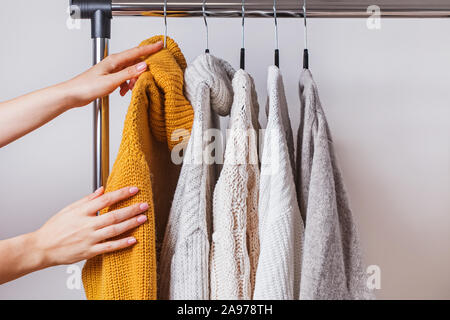 Die Frau Hände Wahl gelb Strickpullover unter anderem auf Kleiderbügel Stockfoto