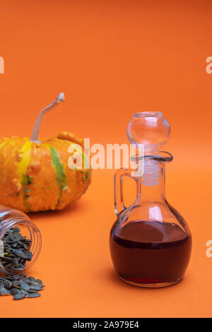 Glas Glas von organischen Kürbiskernöl auf orange Hintergrund Stockfoto