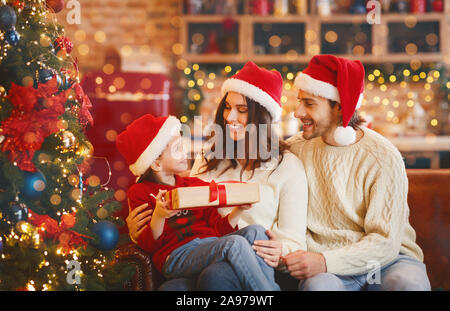Schönen lächeln Eltern in santa Hüte, xmas Geschenk an ihre Tochter, Weihnachten zu Hause feiern, kopieren Raum Stockfoto