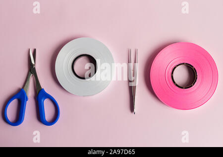 Ribbon Roll auf rosa Hintergrund mit Schere und Pinzette Stockfoto