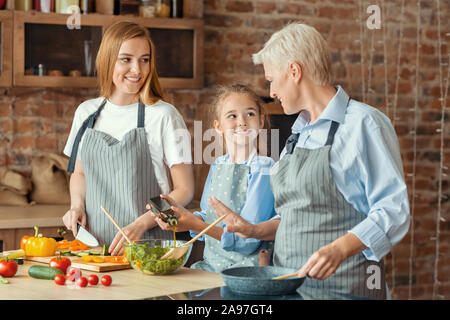 Kleines Mädchen glücklich, Mutter und Großmutter Kochen gesund Abendessen helfen, mischen Salat, Küche Innenraum Stockfoto
