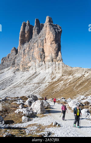 Vier Touristen gehen unter die Südwand der Tre Cime di Lavaredo / Drei Zinnen, Berggipfel in der Sexten Dolomiten, Südtirol, Italien Stockfoto