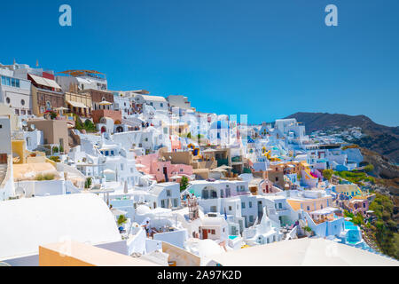 Oia, Santorini, Griechenland - 7. August 2019; Hügel Häuser und Gebäude in Weiß mit Farbakzenten im traditionellen griechischen Stil der Insel mit Tour Stockfoto