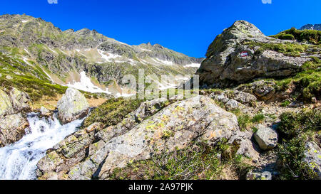 Einen heiteren Blick auf die schneebedeckten Berge von einem kleinen Bach. Der Strom geht auf steilen Steinen, sein Wasser sprudelnd. Hoch aufragenden Gletscher Stockfoto