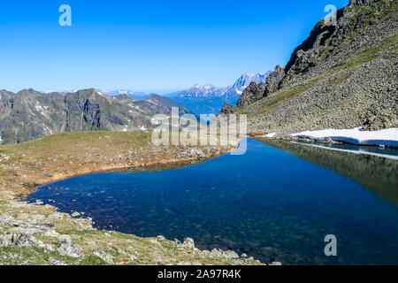 Klar, Navy Blue Lake versteckt zwischen hohen Gipfeln. Einige der Pisten sind noch mit Schnee bedeckt. Auf der Rückseite ist hier eine andere Bergkette. Stockfoto