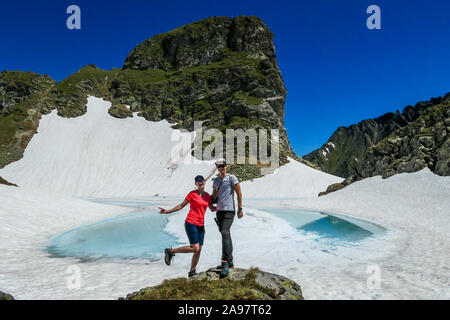 Ein Paar genießt die Aussicht einer gefrorenen Bergsee. Das Eis scheint in vielen verschiedenen Blautönen. See ist von hohen Bergen umgeben. Kein Schnee auf der Stockfoto